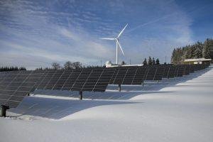 Solar panels and wind turbine in a snowy landscape, showcasing renewable energy sources.
