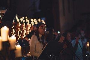 A group of singers performing in a candlelit setting with bokeh lights, creating a warm ambiance.