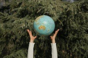 Hands raising a globe against a lush green tree backdrop, symbolizing environmental awareness.